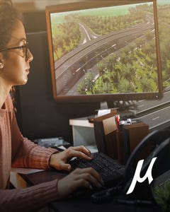 A woman wearing glasses typing on a desktop looking at MicroStation road design. 